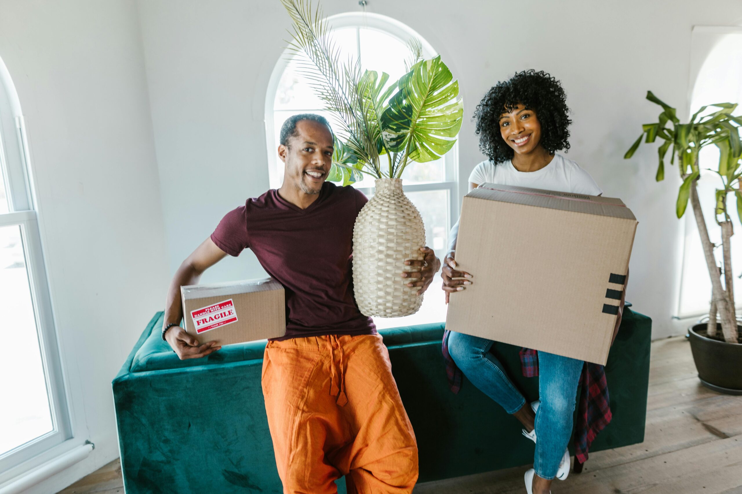 Woman in Purple Long Sleeve Shirt and Orange Pants Holding White Cardboard Box